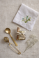Decorative napkin with floral embroidery, gold spoon, and small bottle on a textured surface