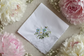 Embroidered handkerchief with floral design on a textured surface with flowers and pearls.
