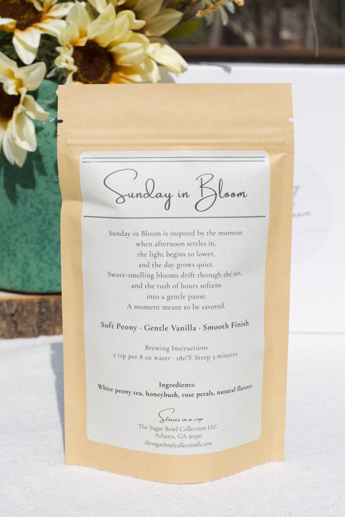 Product packaging with a label titled 'Sunday in Bloom' on a white surface with flowers in the background.